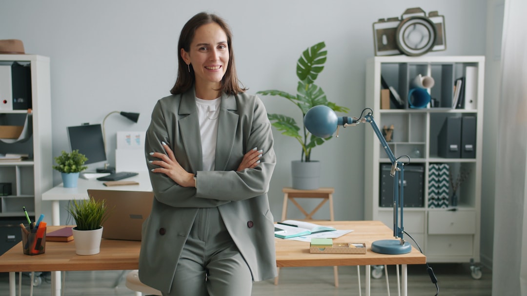 Home portrait of beautiful young businesswoman wearing suit standing alone in office with arms crossed. Modern business, job and people concept.